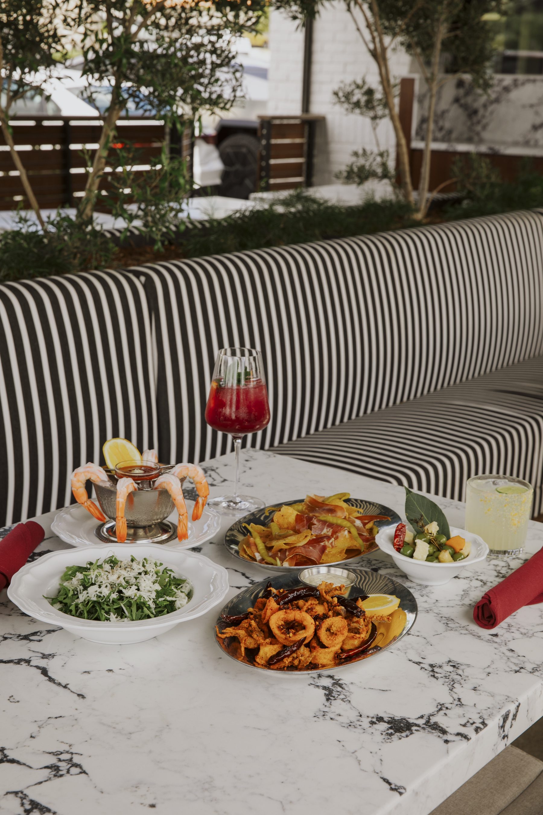 Salina's patio — a striped banquette under olive trees, set with shrimp, calamari and cocktails