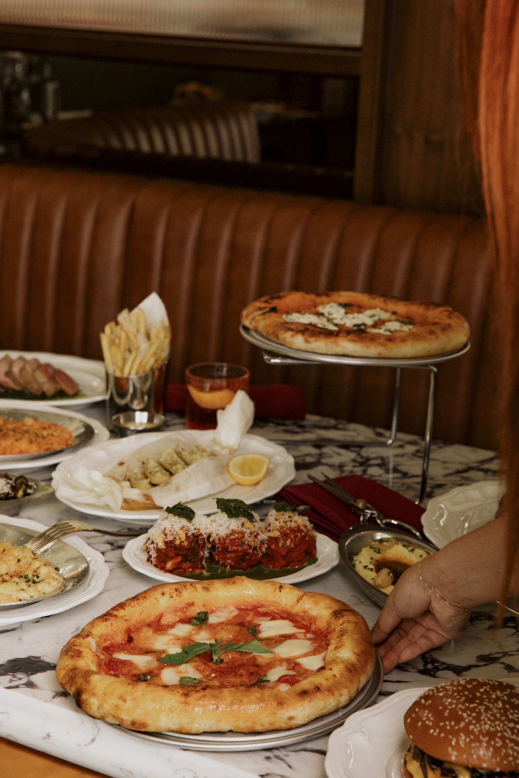 A wood-fired margherita at Salina, with a second pizza on a silver riser and dishes set across the marble table